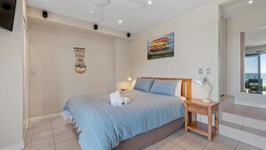 A bedroom with a bed, bedside tables, a wall-mounted artwork, and a view of the sea through a window.
