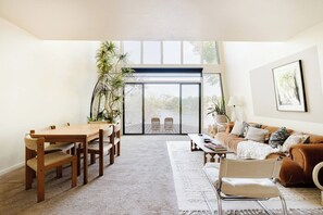 A spacious living room with a dining area, a large sliding glass door leading to a deck, and a comfortable seating arrangement.