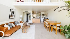 A spacious living area with a brown leather sofa, a wooden dining table, and a kitchen in the background.