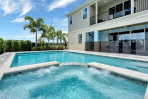 Une piscine avec un jacuzzi, entourée d’un bâtiment à deux étages doté de balcons et de grandes fenêtres.