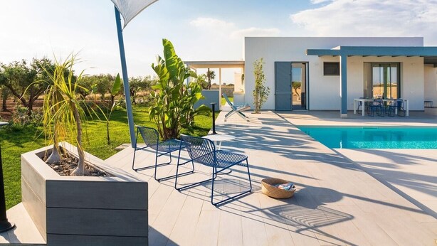 Et moderne poolområde med overdækket siddeområde, en pool og udsigt til et moderne hus.