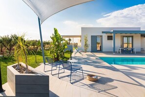 Ett modernt utomhusområde med pool, en pool och en täckt sittplats, samt utsikt över ett modernt hus.