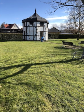 Situated in a serene grassy area, this traditional pavilion offers a tranquil retreat with a distinctive black roof and white timber framing.