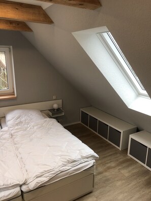 Une chambre avec un plafond en pente, une lucarne, un lit, une table de chevet avec une lampe et des rangements intégrés.