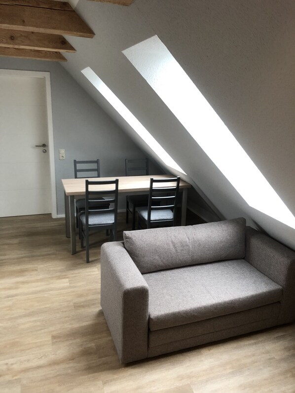 A loft-style room with a wooden dining table and chairs, a grey sofa, and a slanted ceiling with skylights. - Vacation apartment at the stork's nest near the Baltic Sea/Zingst/Darß (Kenz-Küstrow)