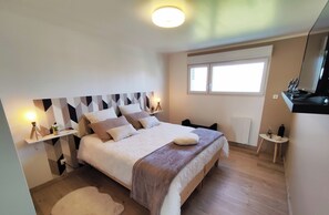 A bedroom with a bed, bedside tables, a nightstand, a window, and a mirror.