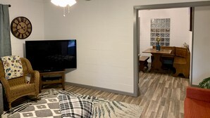 Un salon équipé d’un téléviseur à écran plat, d’un ventilateur de plafond, d’une horloge et d’un coin repas avec une table et des chaises.