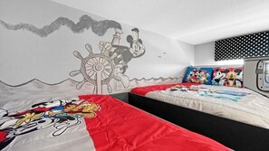 Quarto com duas camas, uma com colcha temática do Mickey Mouse e a outra com almofada da Disney.