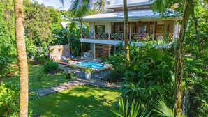 Una casa moderna con piscina, rodeada de exuberante vegetación y palmeras.