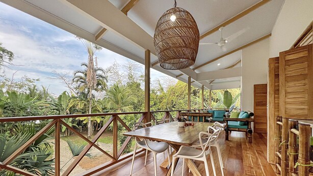 Un comedor amplio con una mesa y sillas de madera, una lámpara colgante y vistas a abundante vegetación.