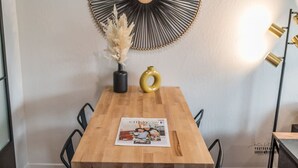 A wooden dining table with a magazine, a vase with dried flowers, and a decorative wall piece.