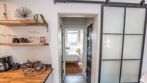 A narrow hallway leading to a bedroom with a bed, a wooden counter with kitchen items, and a frosted glass partition.