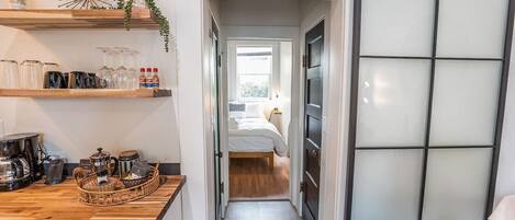Un pasillo estrecho que conduce a un dormitorio con una cama, un mostrador de madera con utensilios de cocina y un panel de vidrio esmerilado.