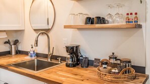 A kitchen with a wooden countertop, a stainless steel sink, a coffee maker, and a hanging mirror.