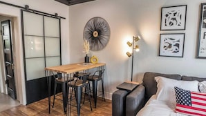 A modern room with a wooden dining table, black chairs, a sofa with an American flag pillow, and abstract wall art.
