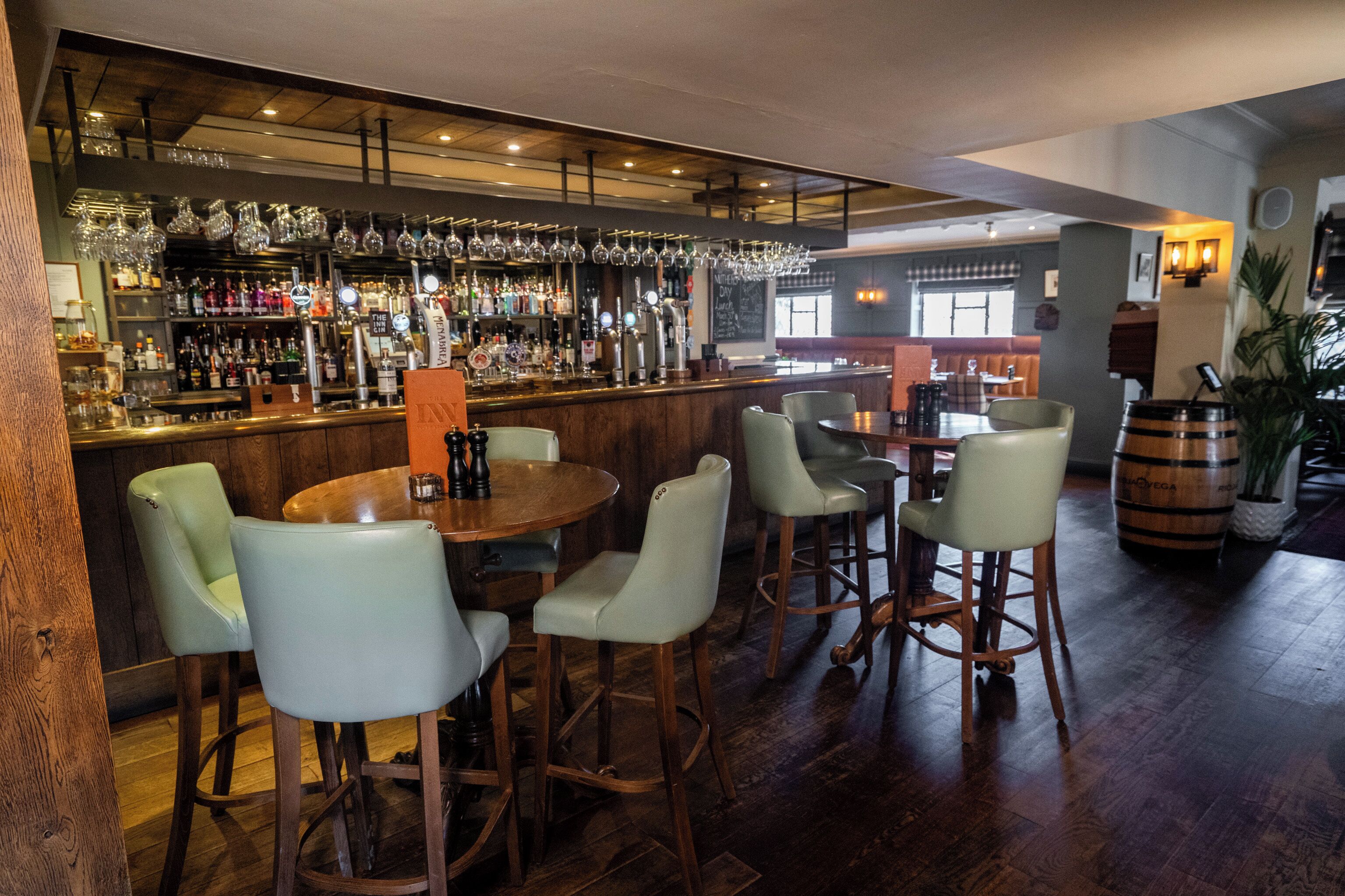 A bar area with stools, a bar counter, and a variety of bottles and glasses.
