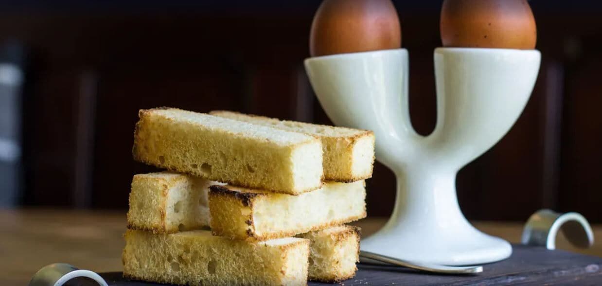 A stack of white bread slices and a white ceramic holder with two brown eggs on top.