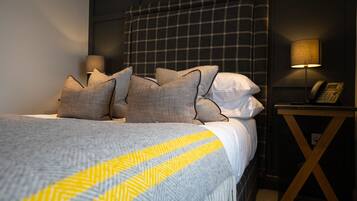 A neatly made bed with a grey and yellow striped blanket, a plaid headboard, and a bedside lamp on a wooden nightstand.