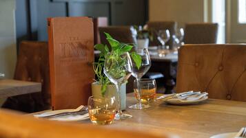 Une table de restaurant mise avec des verres à vin, un menu et une plante en pot.