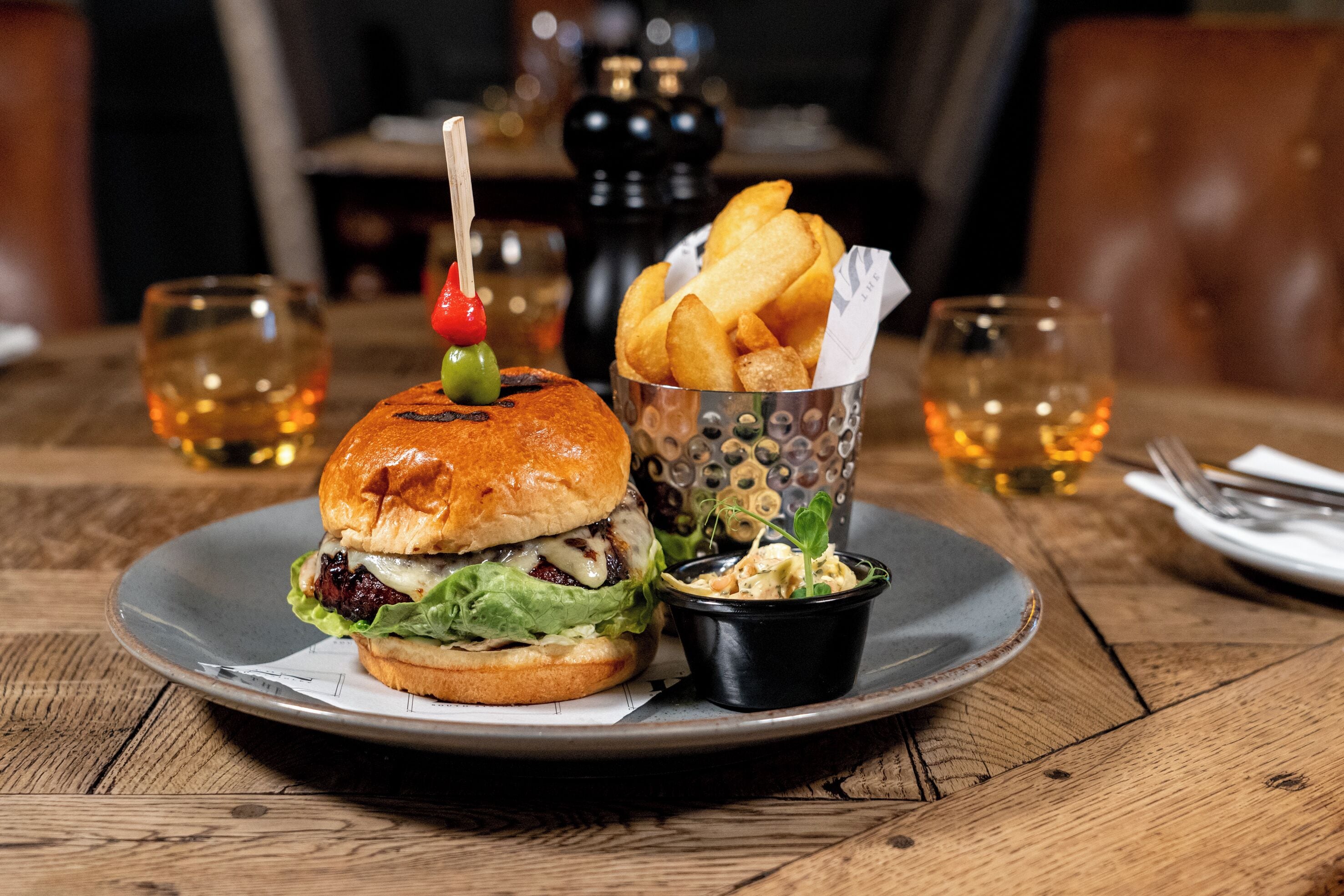 A burger with a toothpick, fries, and a side dish on a plate.