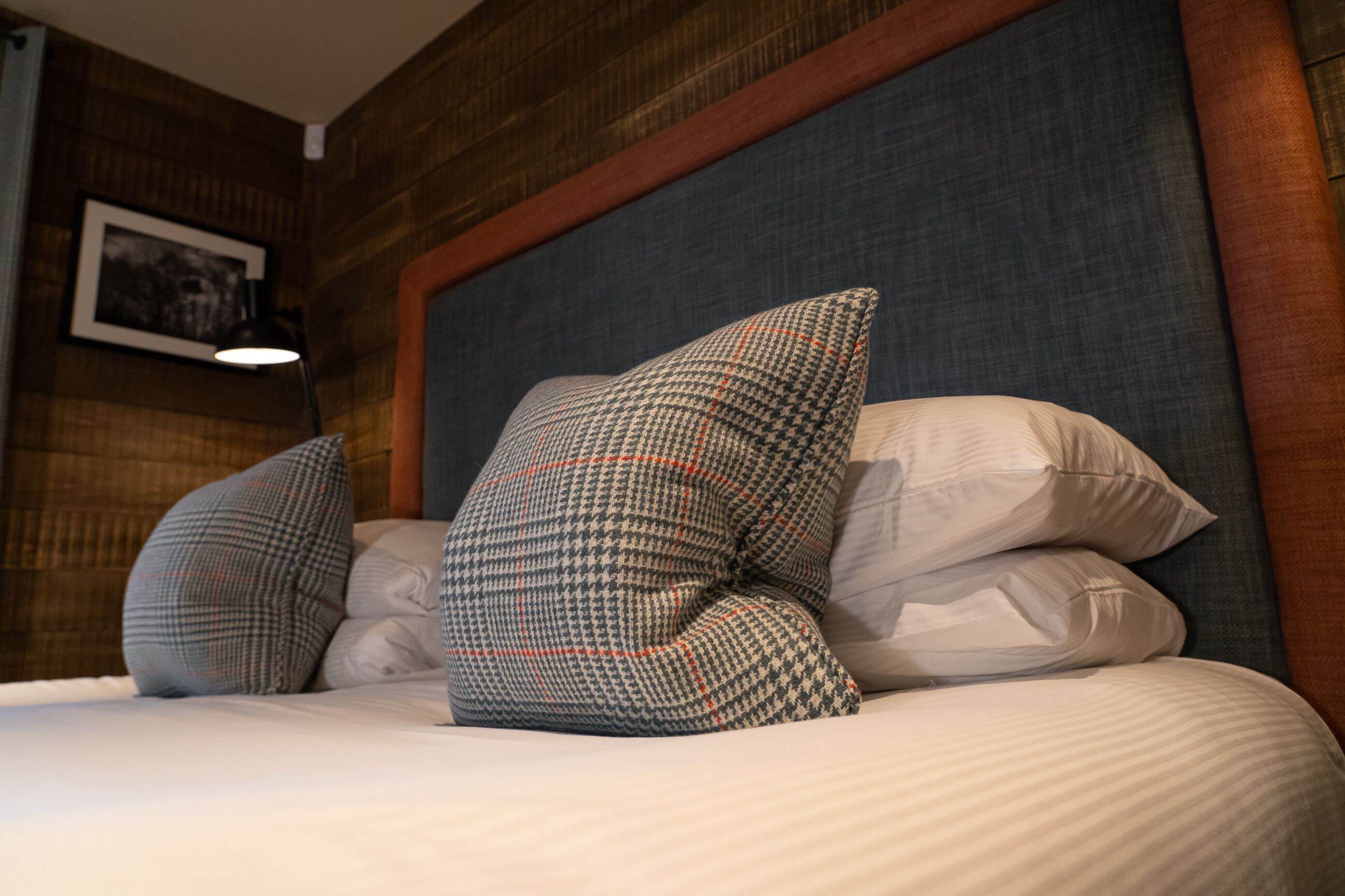 A neatly made bed with patterned pillows and a headboard against a wooden wall.