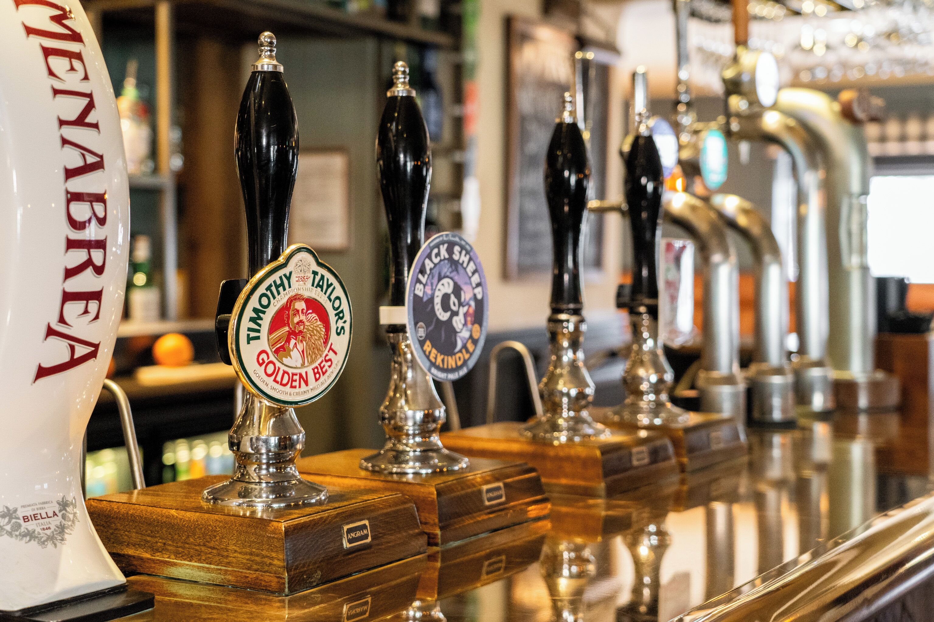 Eine Bar mit mehreren Zapfhähnen, darunter Biersorten wie 'Timothy Taylor's Golden Best' und 'Black Sheep Rekindle'.