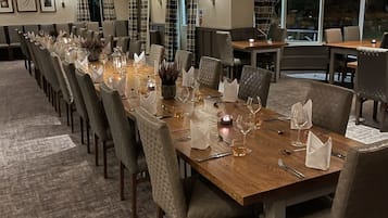 A long dining table set for a formal event, with chairs and table settings including wine glasses and candles.