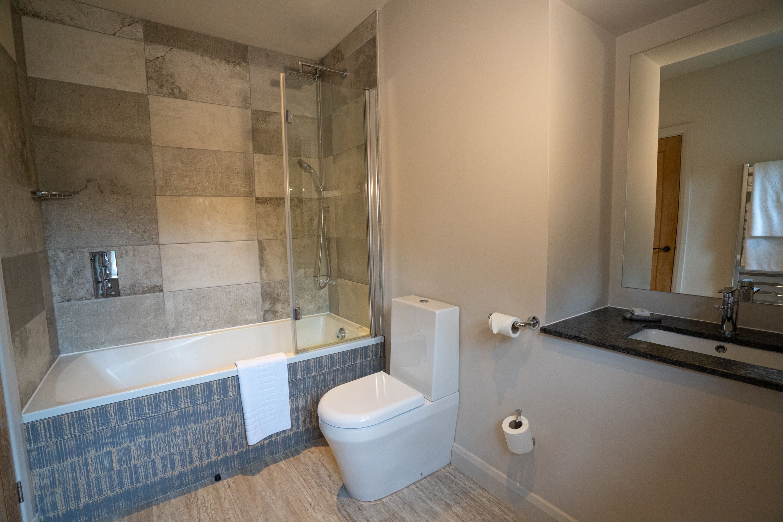 Un baño moderno con ducha acristalada, inodoro blanco y lavamanos con espejo.