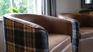A brown leather armchair with a plaid pattern on the backrest, positioned near a window with a view of greenery.