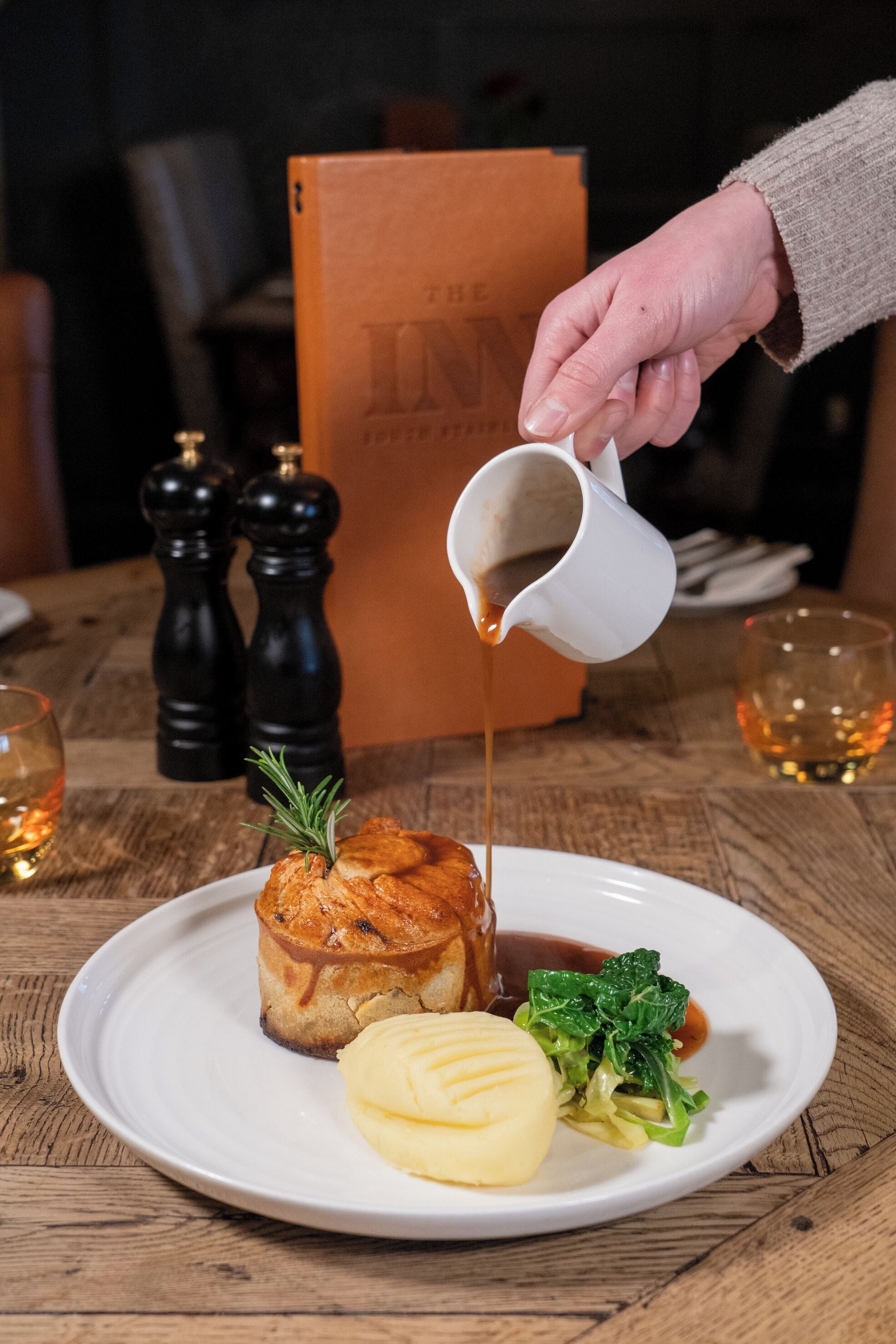 A dessert with gravy on a plate, a sprig of rosemary, and a side of greens.