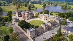 A historic castle with a large courtyard, surrounded by lush greenery and a river. - The Inn South Stainley (Harrogate)