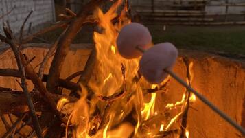 A campfire with logs and branches, and two marshmallows on sticks.