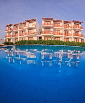 Un hotel con piscina, varios balcones y un cielo azul despejado.
