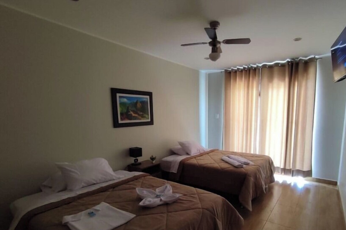 A hotel room with two beds, a ceiling fan, a painting on the wall, and a window with curtains.