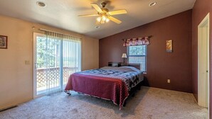 Ein Schlafzimmer mit Deckenventilator, einem Bett mit gemustertem Überwurf, einem Fenster mit Jalousien und einer Tür.