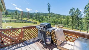 Eine Terrasse mit Grill, Propanflasche und einem Glastisch.