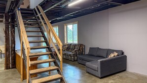 Ein Loft-Zimmer mit einer Holztreppe, einem grauen Sofa und einem gemusterten Sitzsofa.