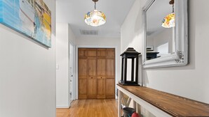 Un couloir avec un plancher en bois, une porte en bois, un miroir, une lanterne suspendue et un tableau accroché au mur.