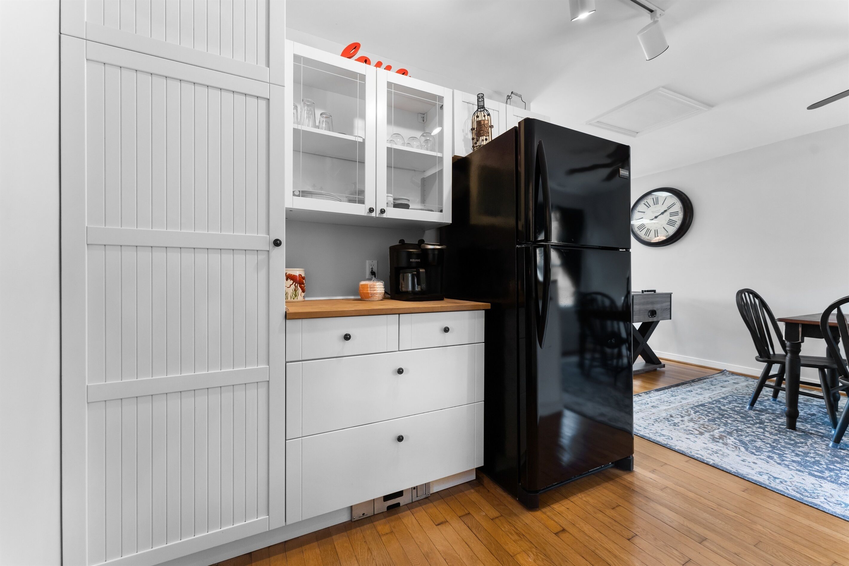 Une cuisine moderne avec des meubles blancs, un réfrigérateur noir et un coin repas comprenant une table et des chaises en bois.