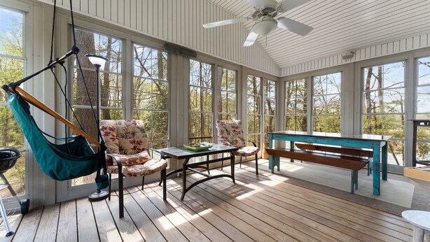 Une véranda avec un plancher en bois, un hamac, une table et des chaises.