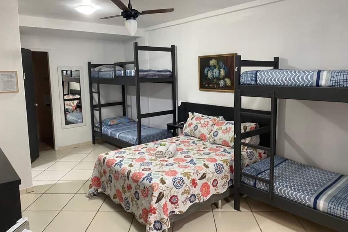 A dormitory room with bunk beds, a ceiling fan, a framed picture on the wall, and a door leading to another room.