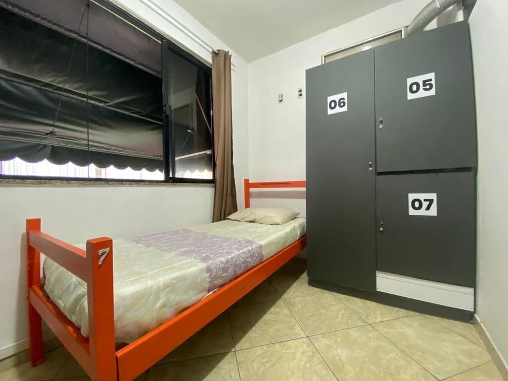 Habitació petita amb un llit individual, un armari i una finestra amb cortines.