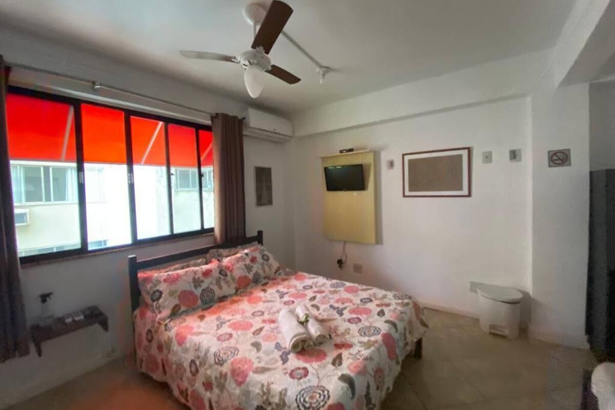 A bedroom with a bed, a ceiling fan, a TV, and a window with curtains.