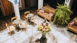 A lobby with a patterned floor, a round table with chairs, a sofa with cushions, and a large green plant.