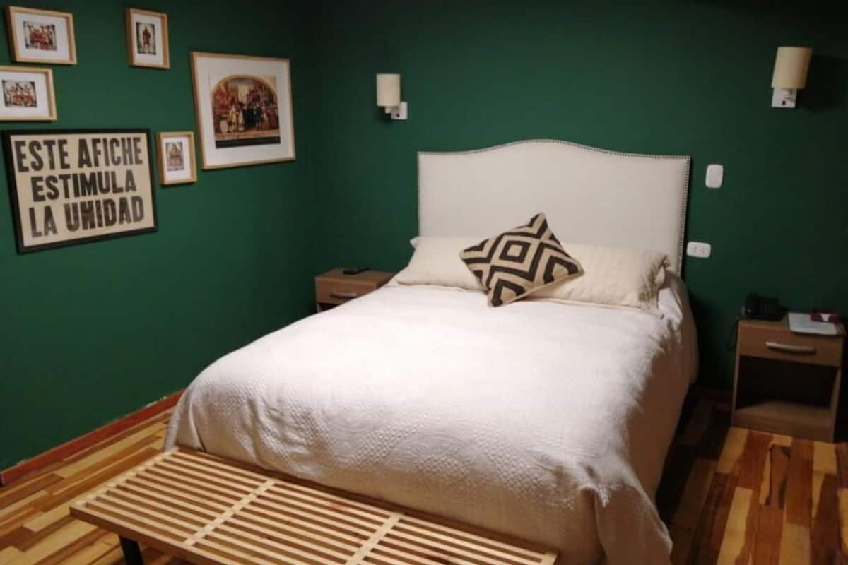A bedroom with a bed, a bench, a nightstand, and framed pictures on the wall.