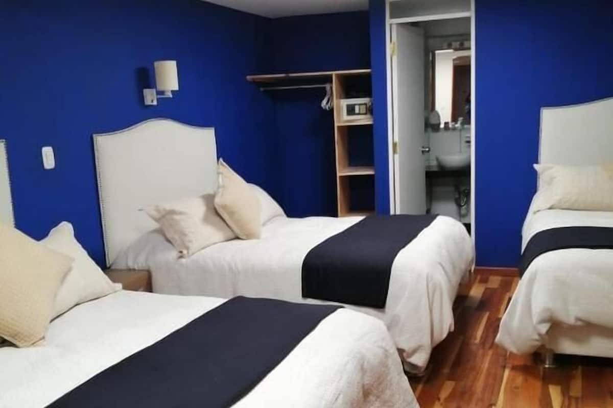 A hotel room with two beds, a wardrobe, and a bathroom visible through an open door.
