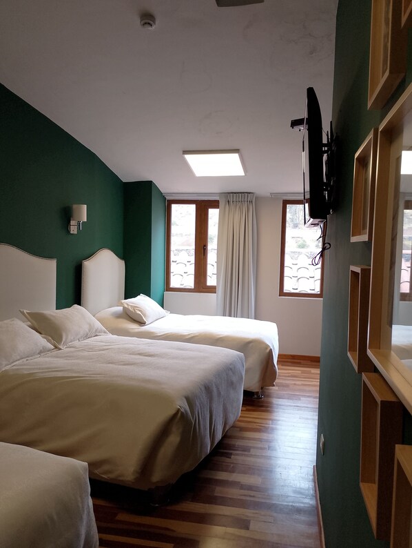 A hotel room with two beds, a flat-screen TV mounted on the wall, and a window with curtains.