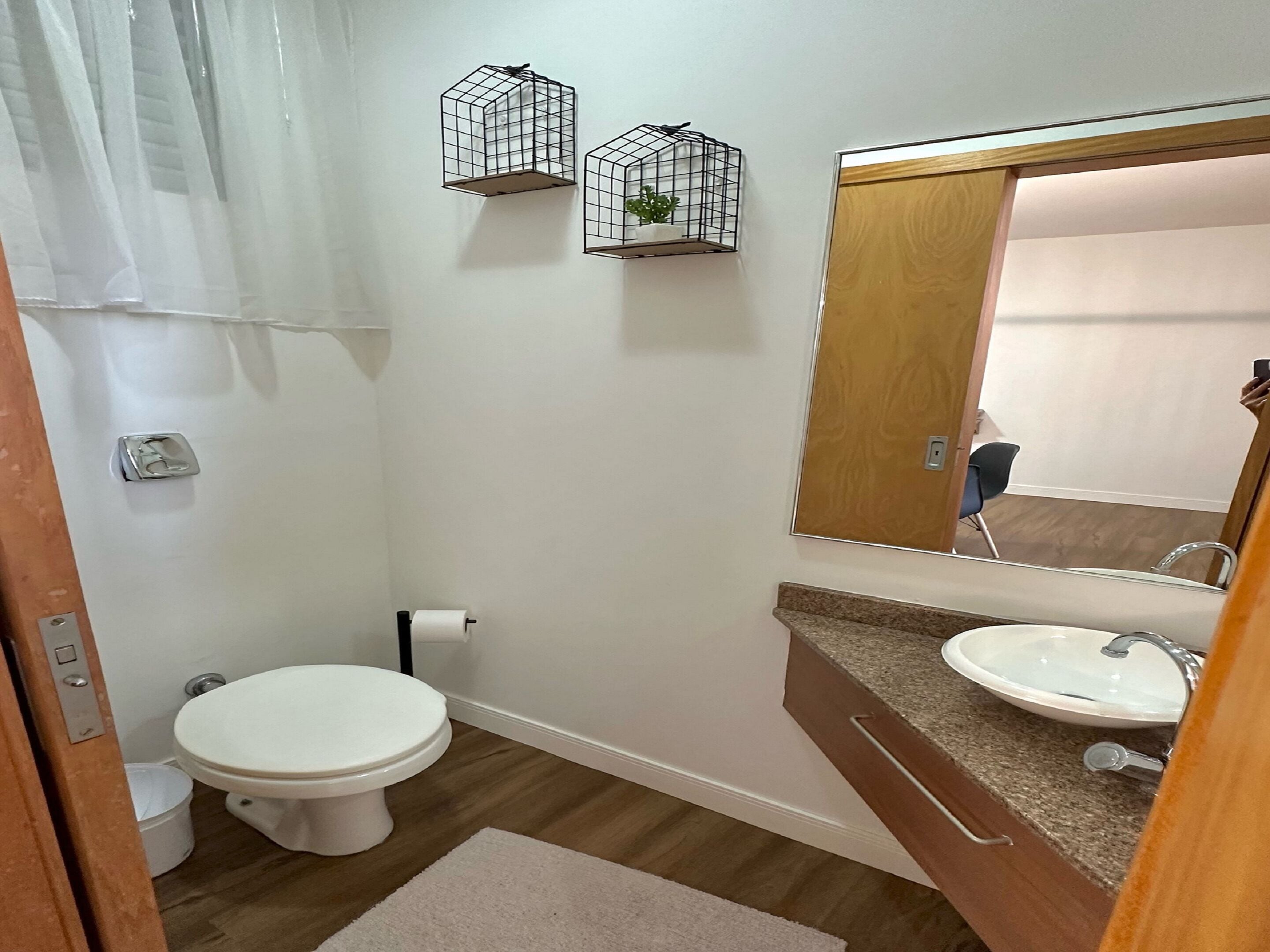 Un baño con inodoro, lavamanos y espejo. Hay dos jaulas colgantes con plantas.