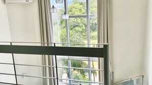 A room with a large window, a ceiling fan, and a view of greenery outside. - Apartamento 206 Saint Sebastian Flat Duo (Jaragua do Sul)