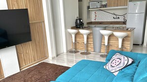 A modern living room with a large sofa, a flat-screen TV, and a kitchen area with bar stools. - Apartamento 206 Saint Sebastian Flat Duo (Jaragua do Sul)